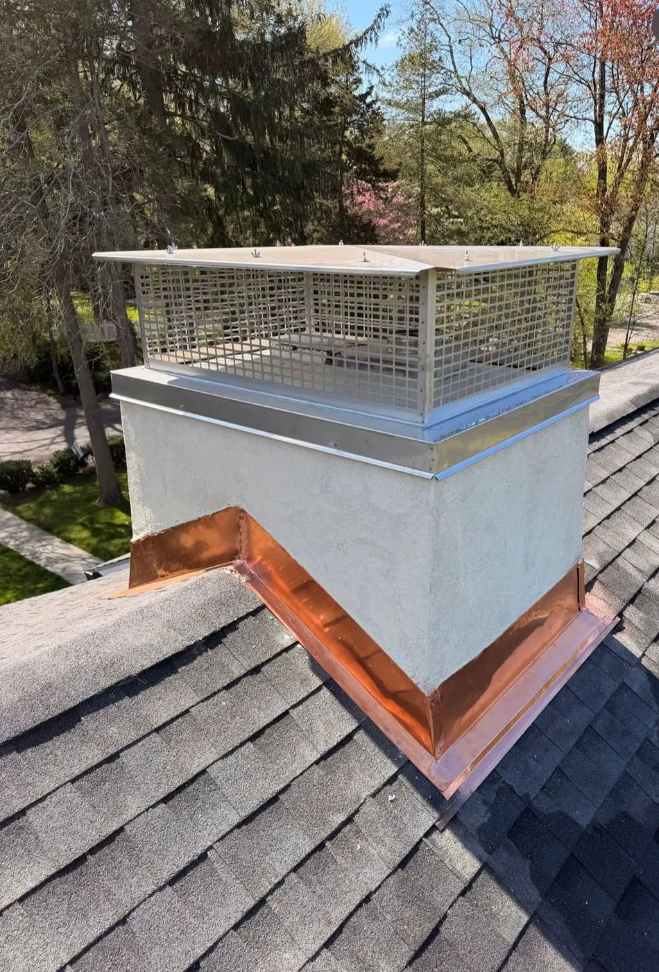 Stainless steel chimney cap and new copper base flashing on a freshly parged chimney