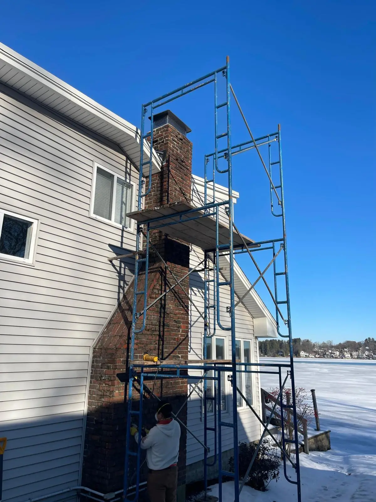 Worker repointing a brick chimney on scaffolding in the South Shore