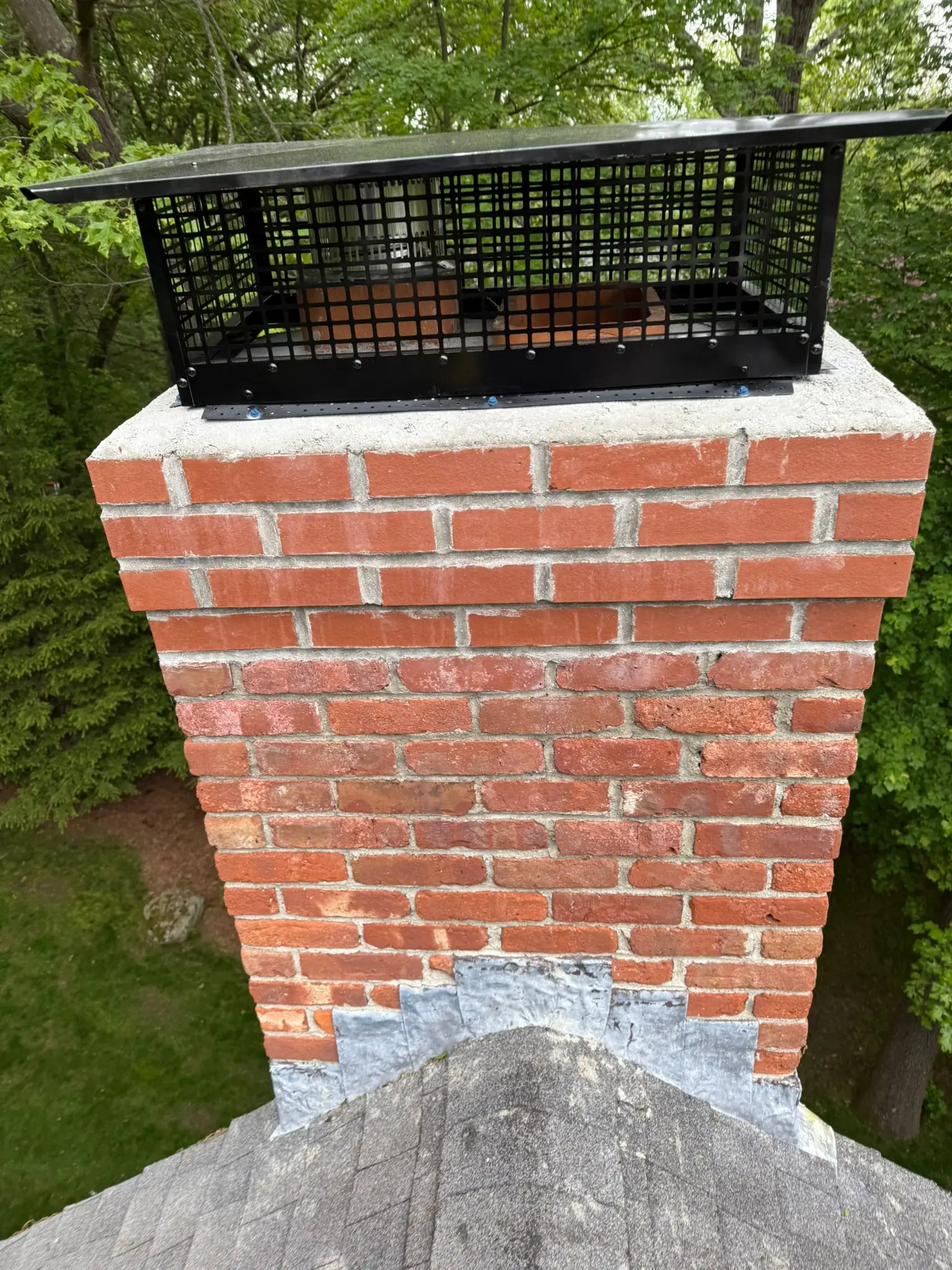 Black multi-flue chimney cap installed on a tall brick chimney