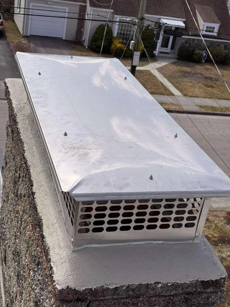 Large stainless steel chase-style chimney cap installed on a wide chimney
