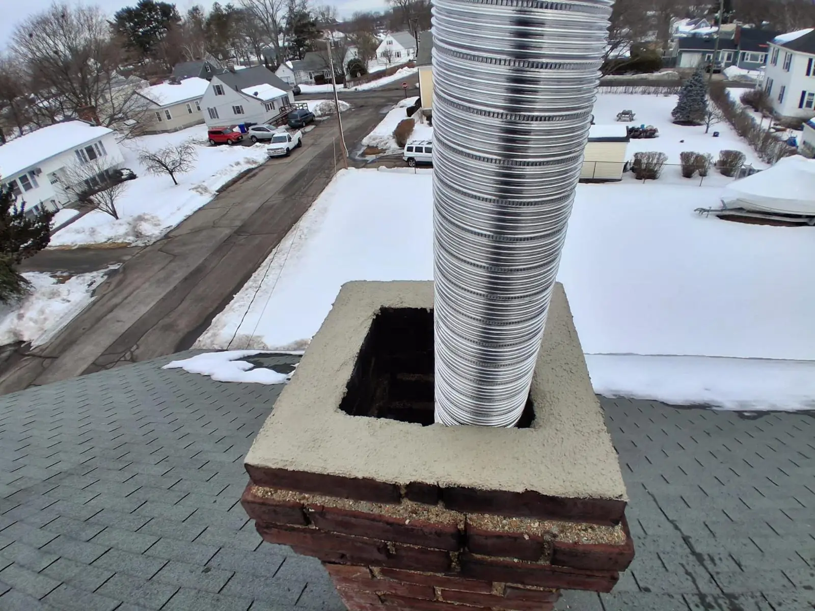 Stainless chimney liner exiting a freshly rebuilt brick chimney crown in winter