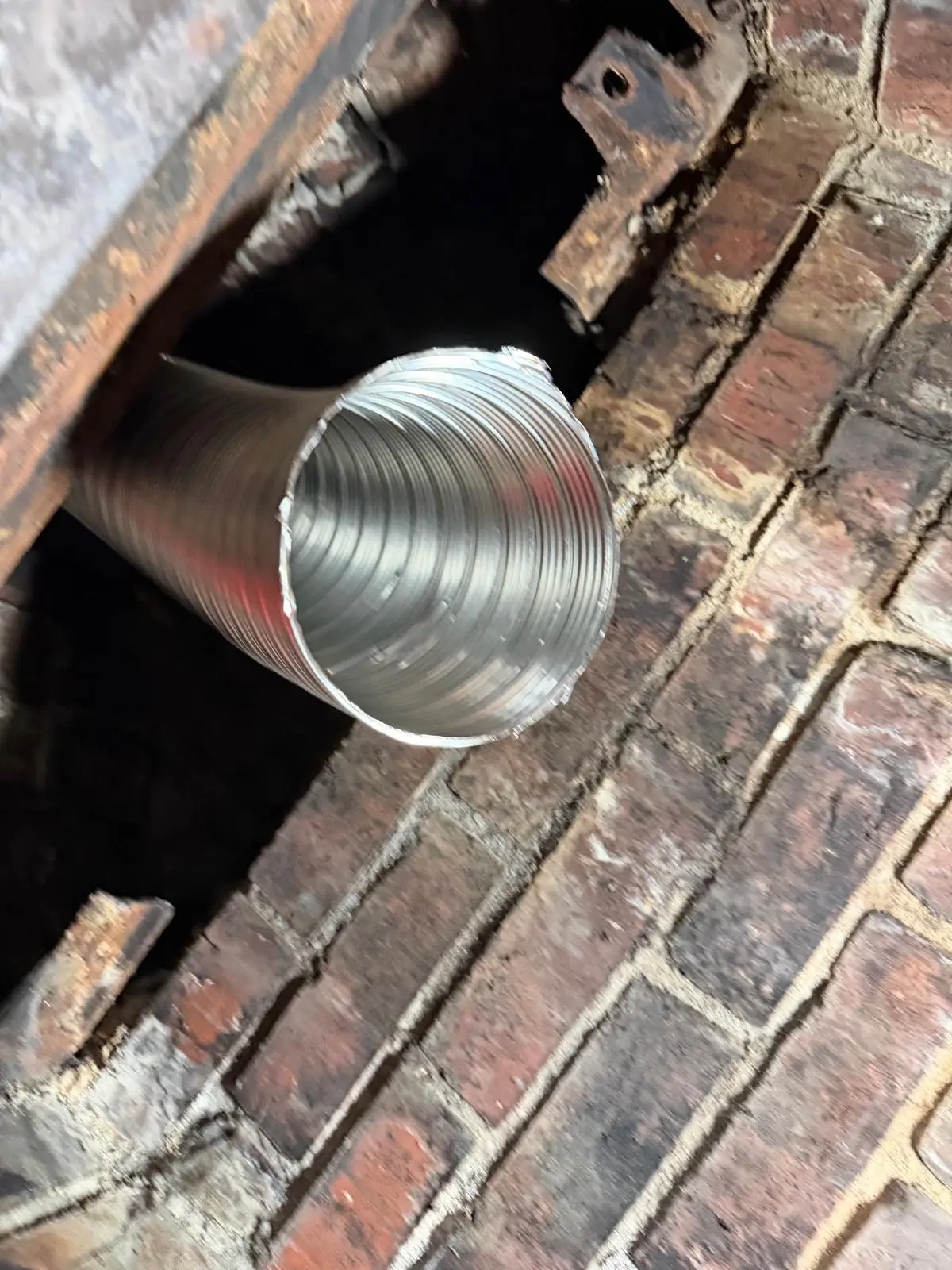 Stainless flex chimney liner coming through a damper into a fireplace firebox
