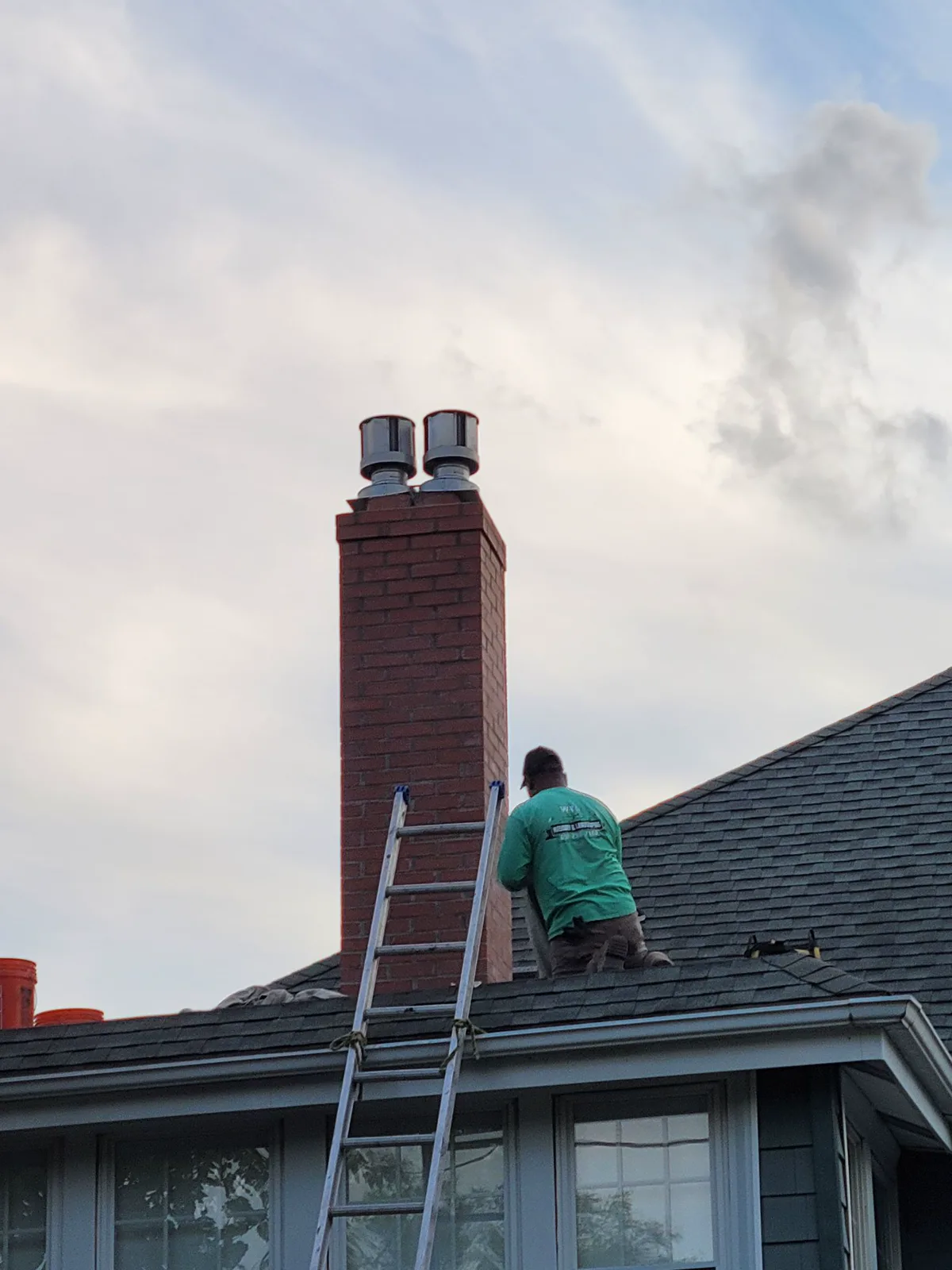 Chimney Goat technician on the roof beside a repaired brick chimney with stainless caps